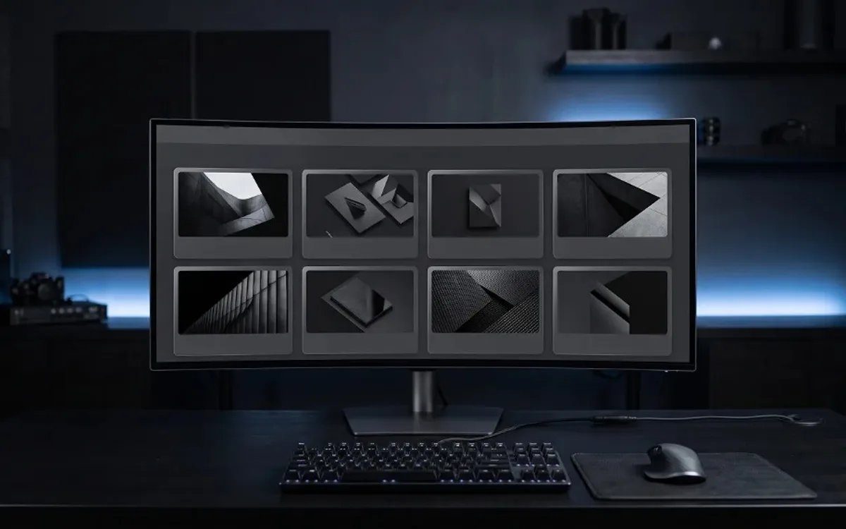Minimalist dark workspace with an ultrawide monitor displaying a gallery of abstract geometric artwork on a desk with blue ambient lighting.